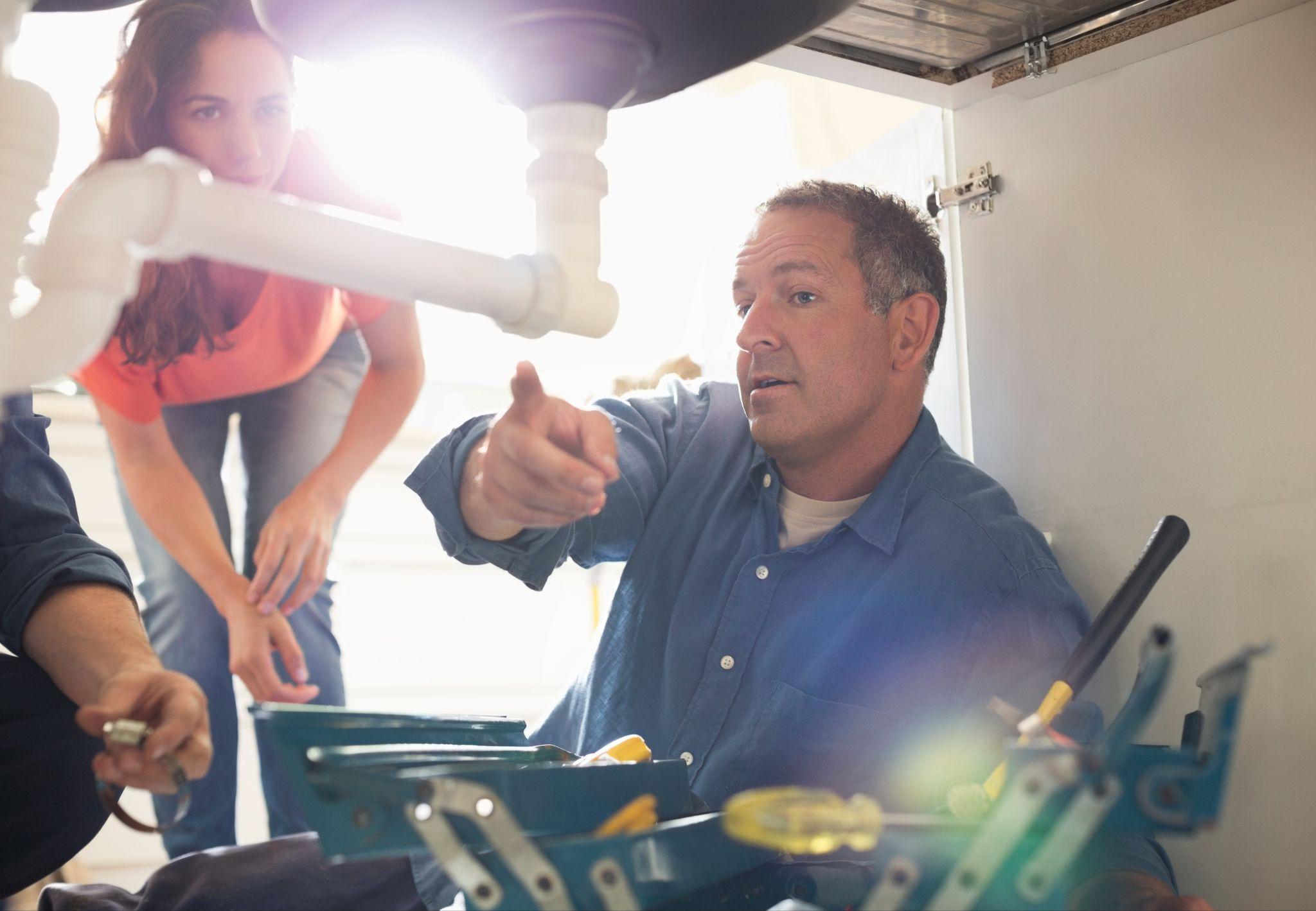 A plumbing technician shows the home owners where the issue with the pipe was